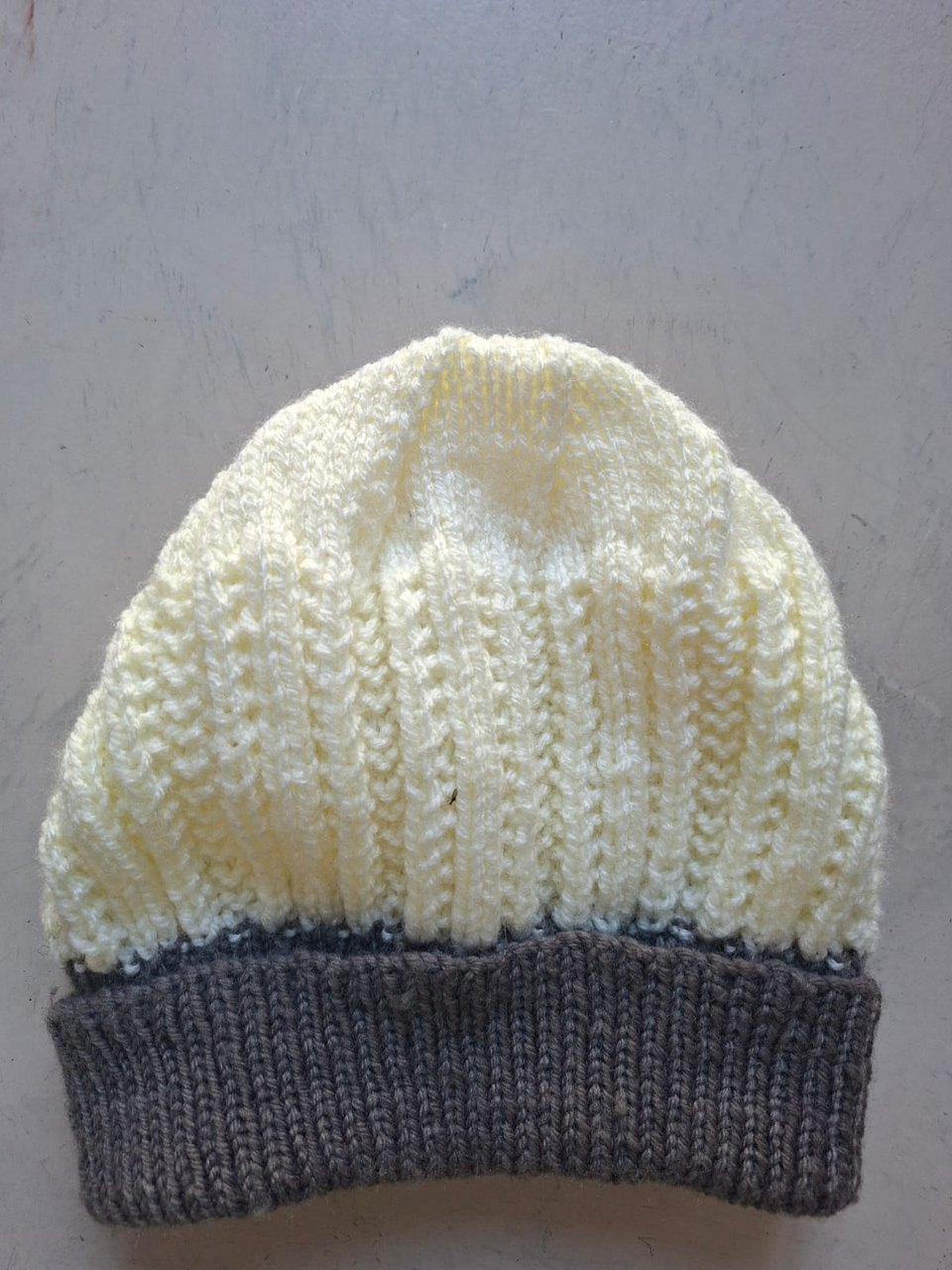 Cream beanie with a charcoal grey cuff, hand-knitted at Kranshoek