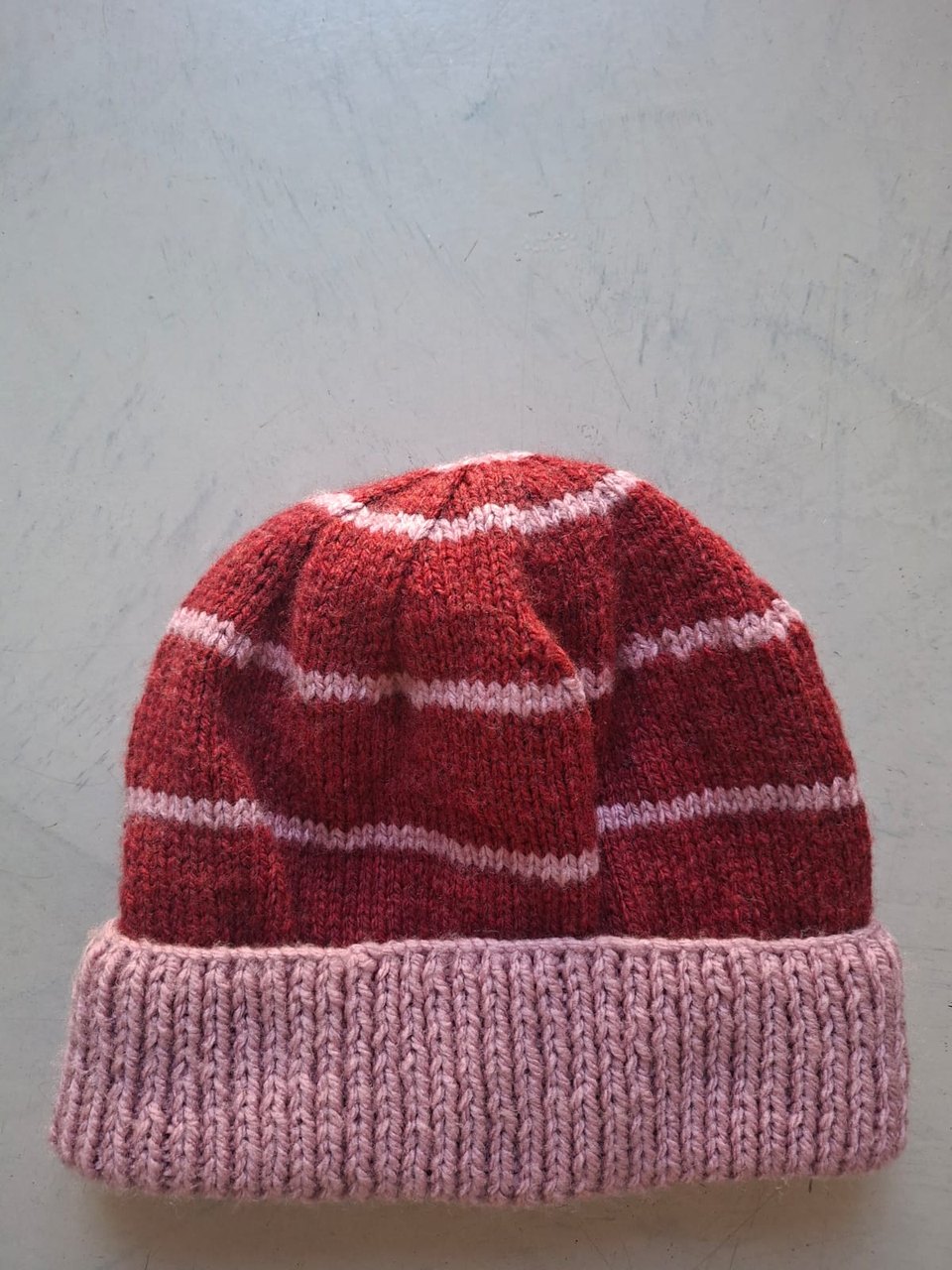 Red beanie with fine pale pink stripes and a dusty pink cuff, hand-knitted at Kranshoek
