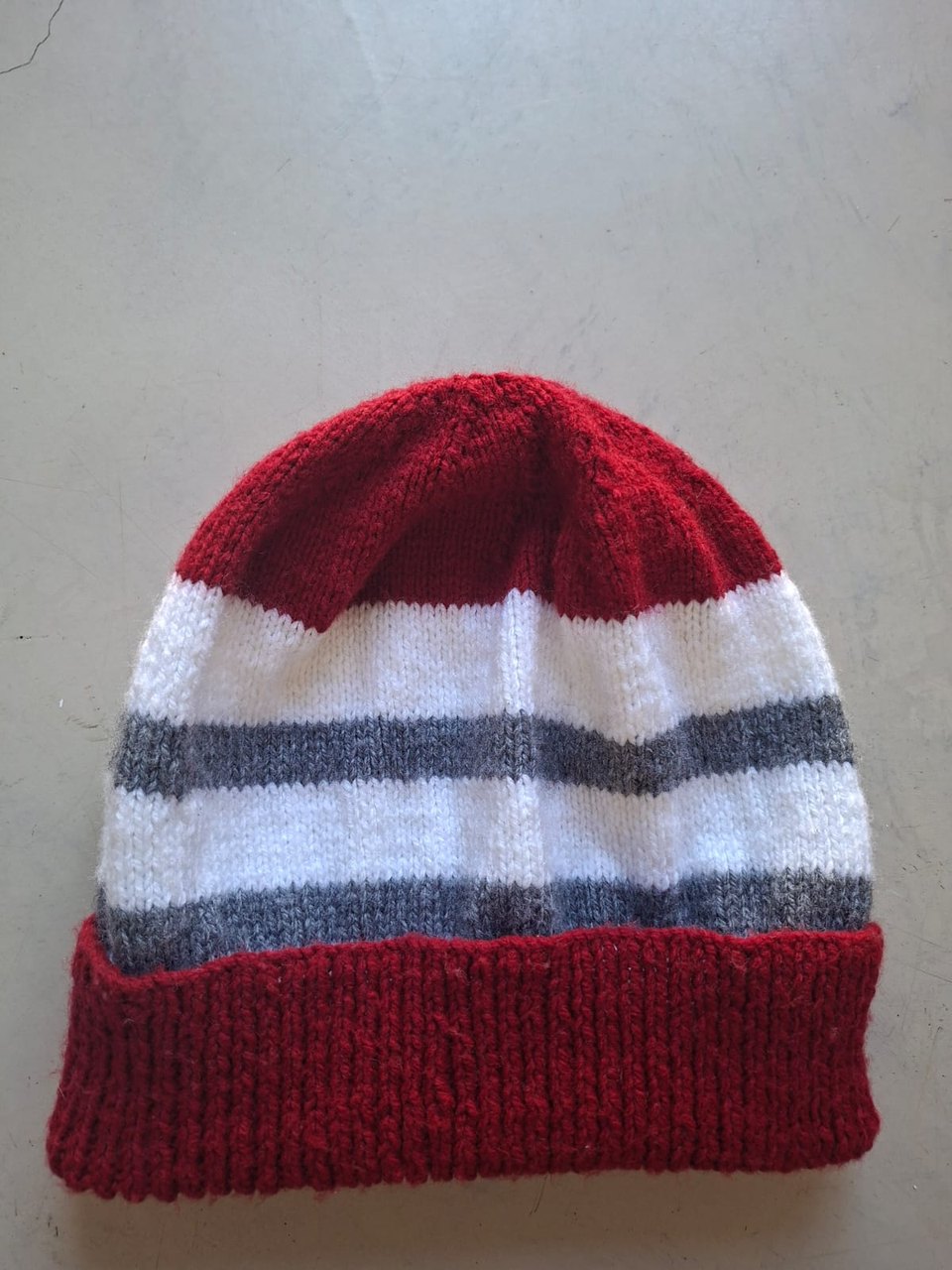 Red beanie with white and grey bands, hand-knitted at Kranshoek