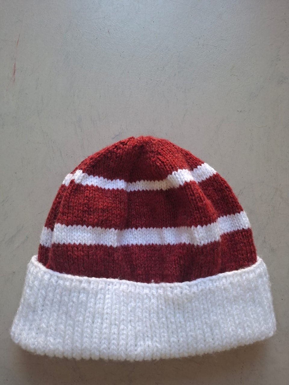 Deep red beanie with white stripes and a white cuff, hand-knitted at Kranshoek